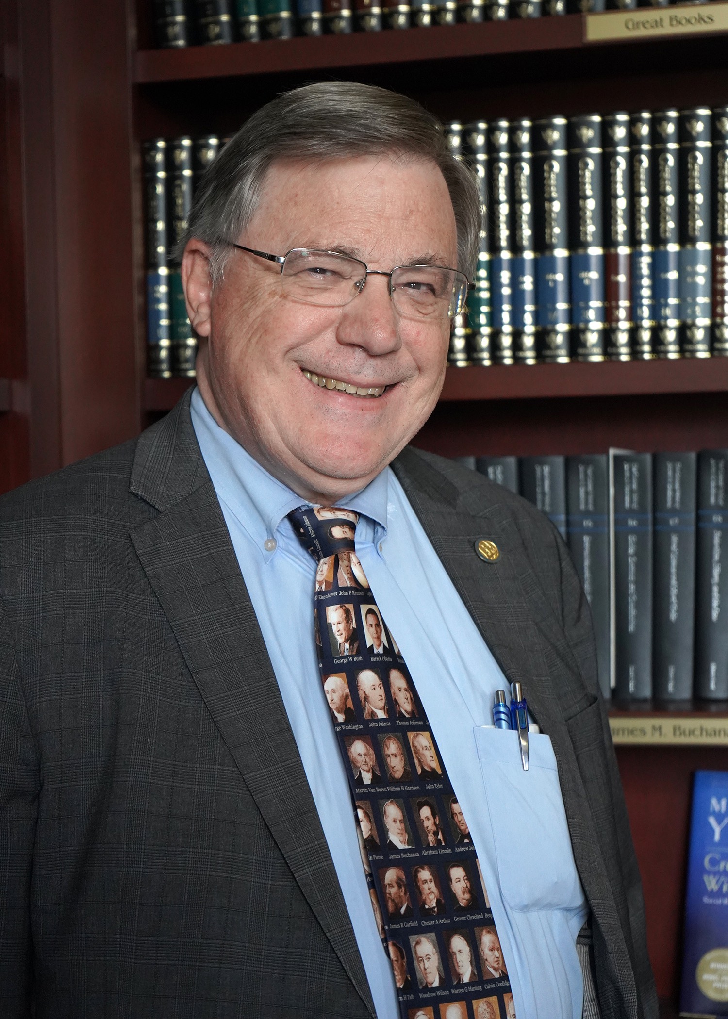 man in suit and tie with glasses standing in front of bookshelf